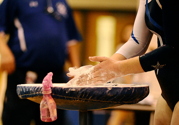 A West Potomac student puts chalk on her hands before her turn on the uneven bars during a meet at West Potomac High School on January 3, 2011.